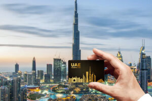 Une main tient une carte de Golden Visa devant la skyline de Dubai. Comment obtenir le Golden Visa ?