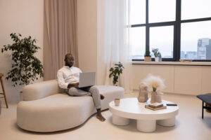 Un homme assis sur son canapé lit un article sur son ordinateur qui traite des erreurs à éviter lors de son premier achat immobilier à Dubaï.